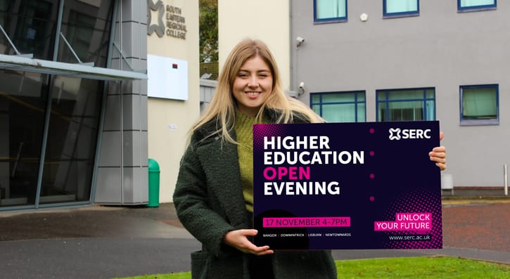 Hope standing outside serc's Newtownards campus holding the HE open evening graphic